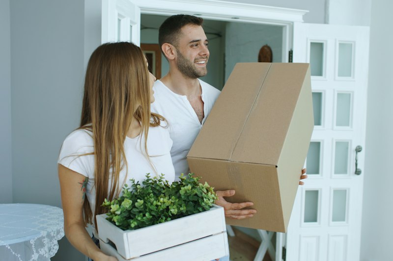 Couple carrying moving boxes through the doorway of their next Utah home